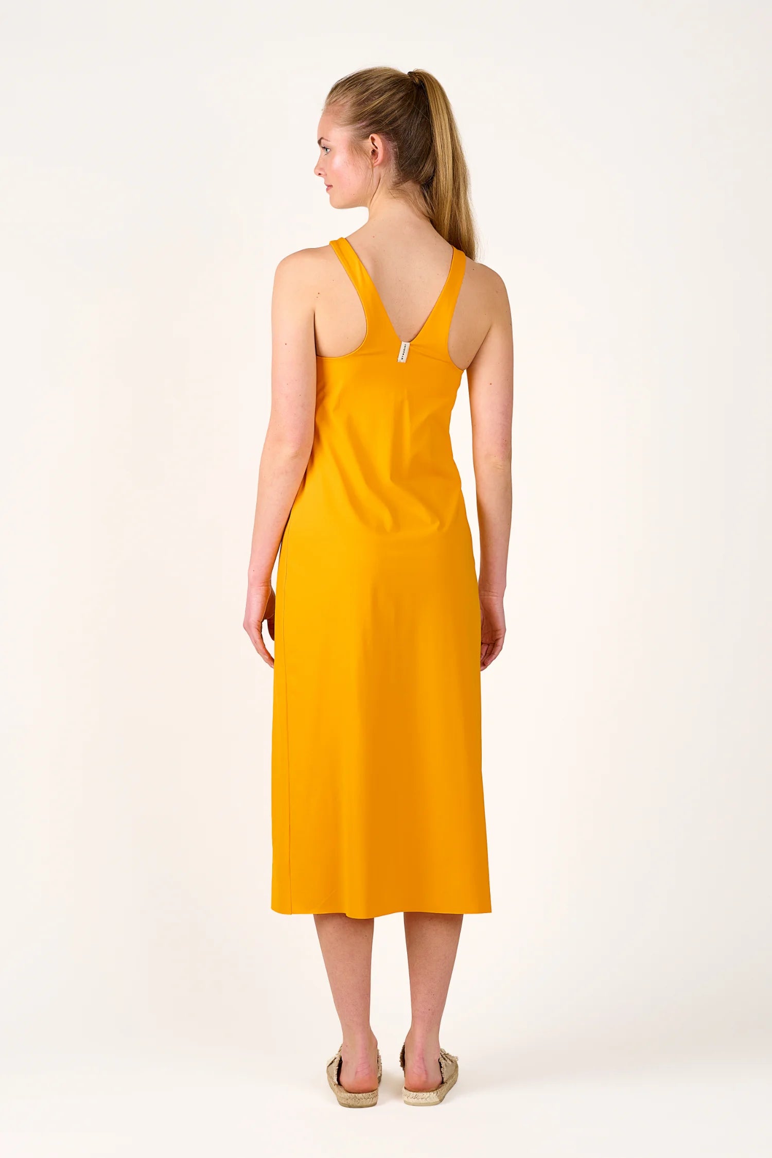 Person in gelbem MYMARINI-Kleid mit breiten Trägern, von hinten gezeigt, steht vor hellem Hintergrund.#color_buttermilk-soleil